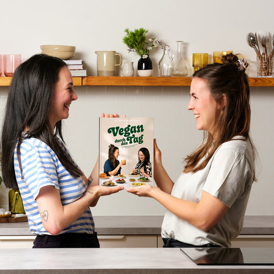 Die Gründerinnen von Zucker & Jagdwurst, Isa & Julia, halten das Kochbuch “Vegan durch den Tag” in der Hand