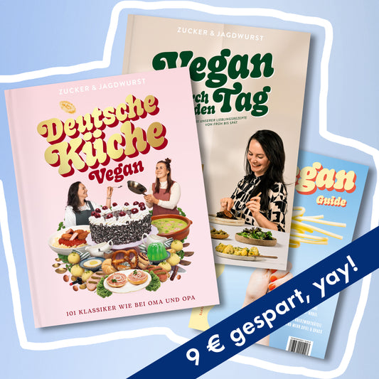 Drei Kochbücher: links vorne ‚Deutsche Küche Vegan‘ mit rosa Cover, in der Mitte ‚Vegan durch den Tag‘ mit beigem Cover und dunkelgrünem Schriftzug, rechts hinten ‚Pasta Guide‘ mit blauem Cover und gelbem Schriftzug, rechts unten mit blauem Spar-Banner