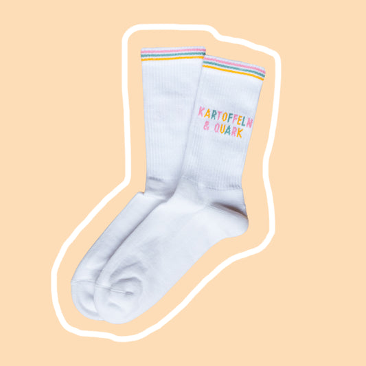 Weiße Tennissocken mit buntem Schriftzug ‚Kartoffeln & Quark‘ auf beigem Hintergrund mit weißer Umrandung