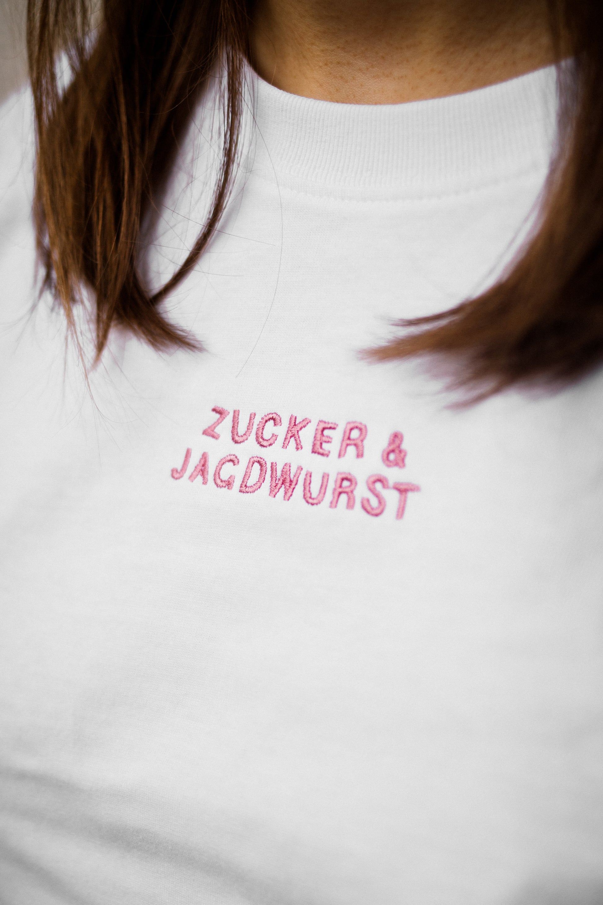 Detailaufnahme vom weißen T-Shirt mit pinker Stickerei “Zucker&Jagdwurst” 